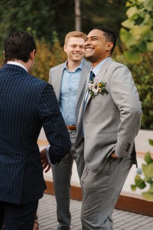 Wedding party members in formal attire share joyful laughter and conversation on an outdoor wooden deck.