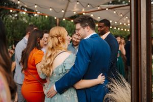 Couples dance together at an outdoor wedding reception under string lights at dusk.