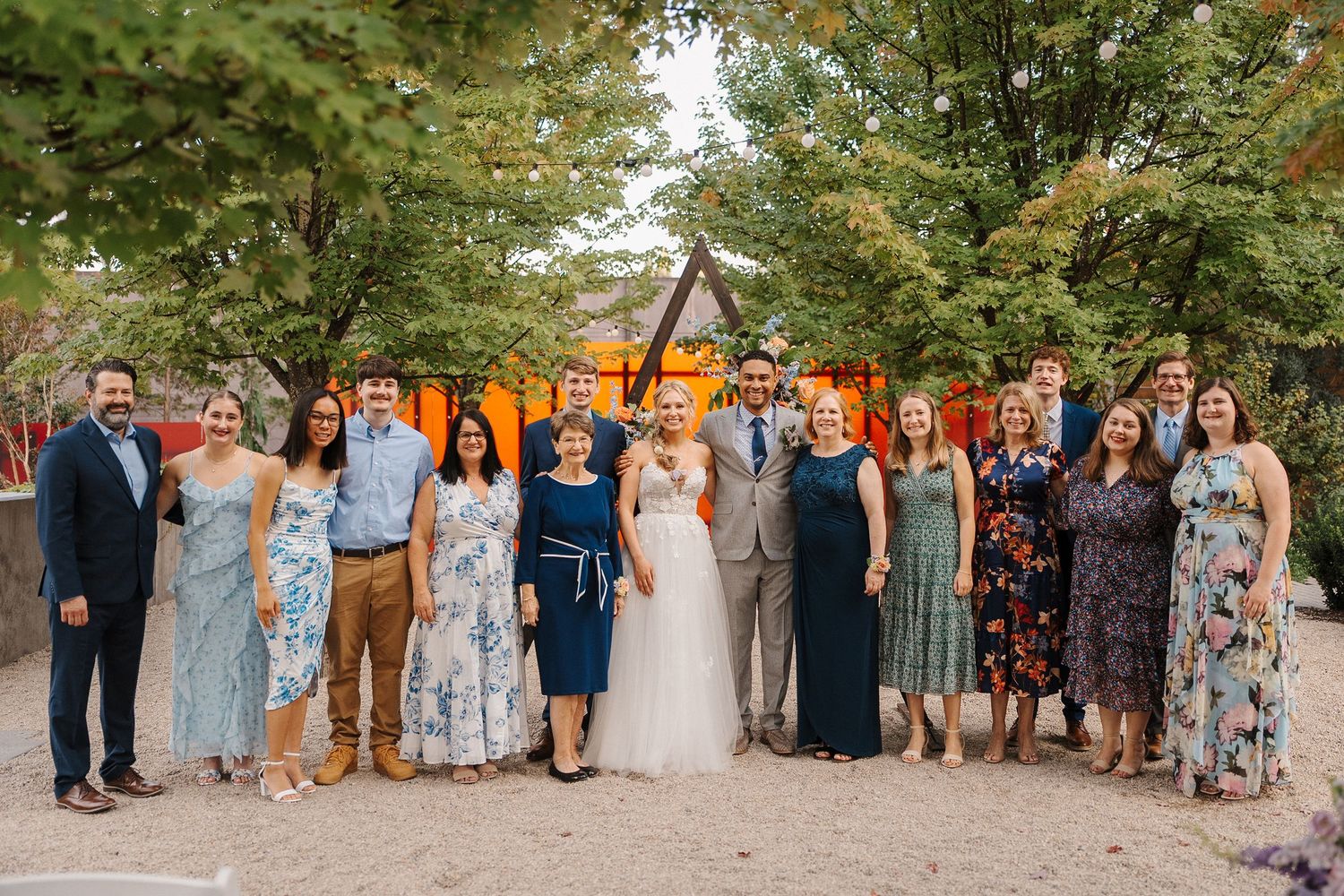 Wedding party in formal attire poses together outdoors with autumn trees and orange decor in the background.