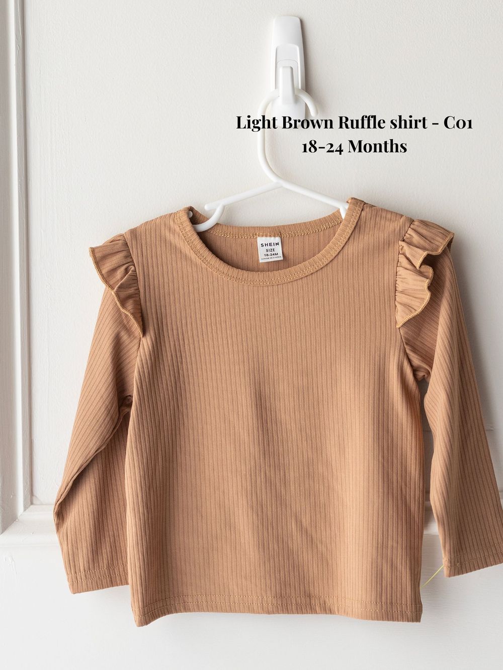 Light brown ribbed cotton toddler shirt with ruffle shoulder details and long sleeves on white hanger, size 18-24 months.