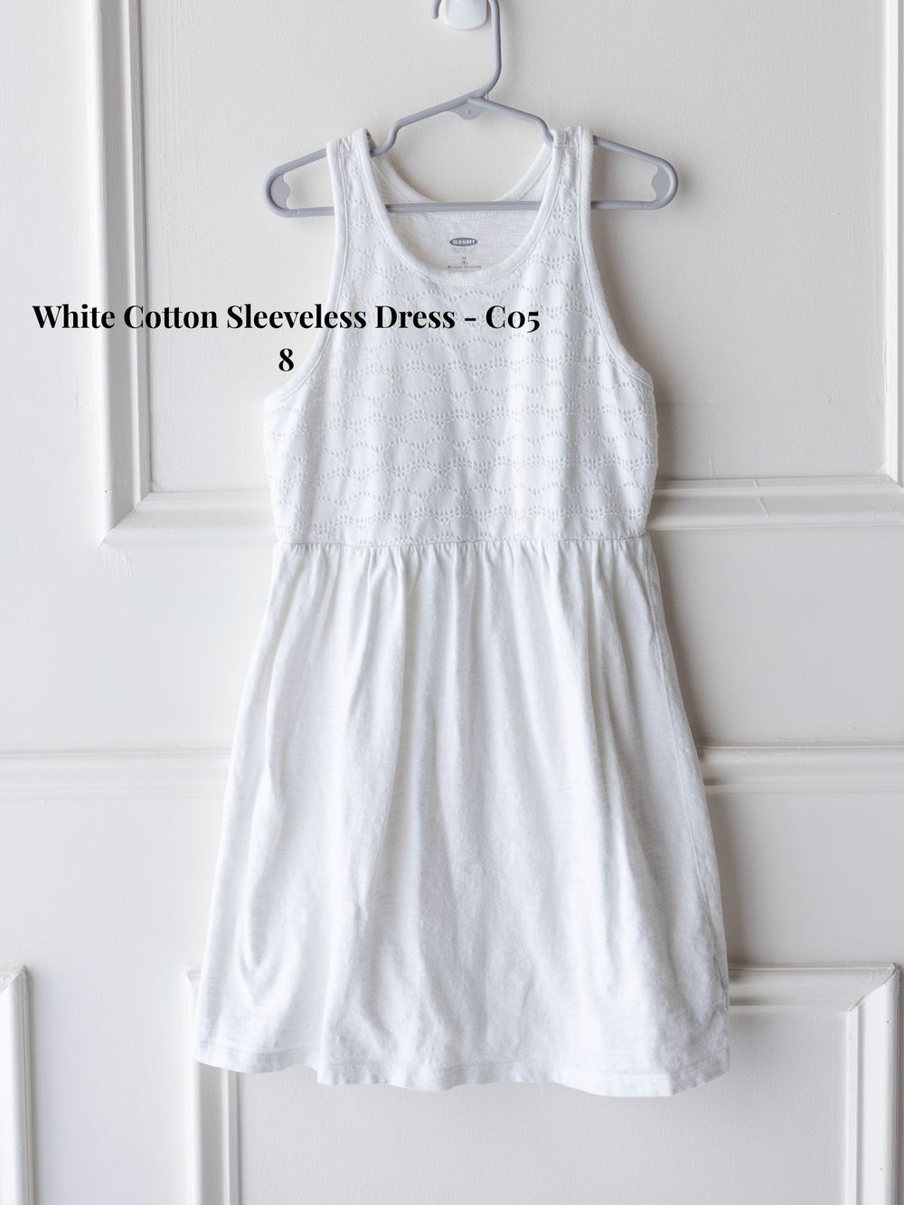 White cotton sleeveless summer dress with empire waist displayed on a hanger against a light background.