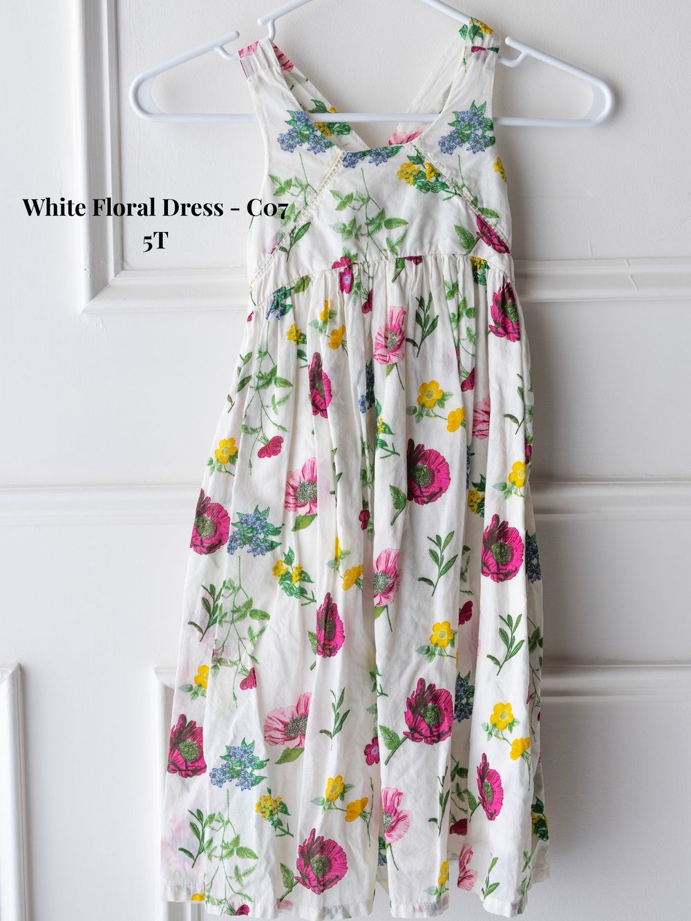 White floral sundress with pink and yellow blooms pattern displayed on white hangers against light background.