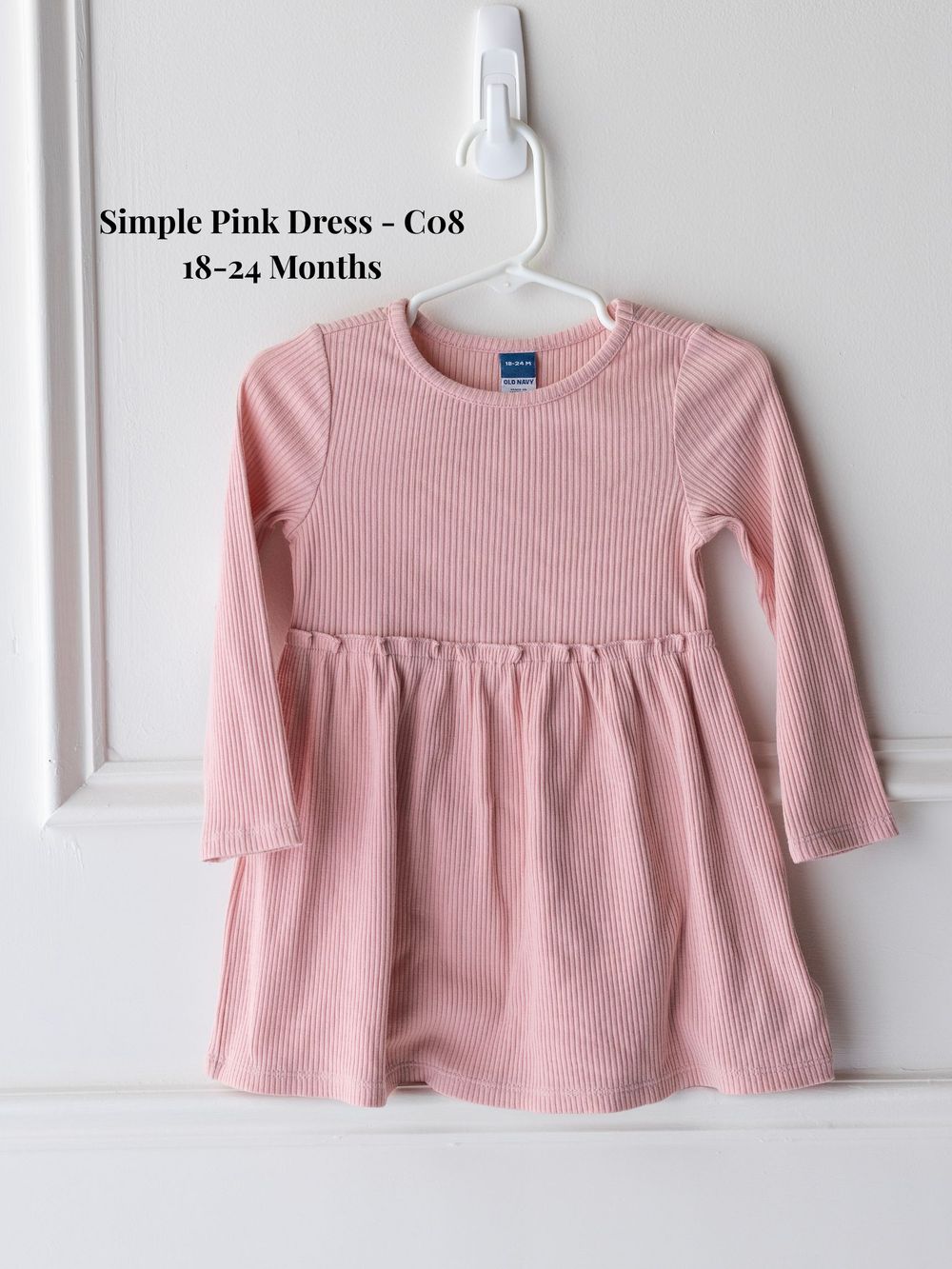 Simple pink ribbed cotton dress with long sleeves and gathered empire waist shown flat on white background.