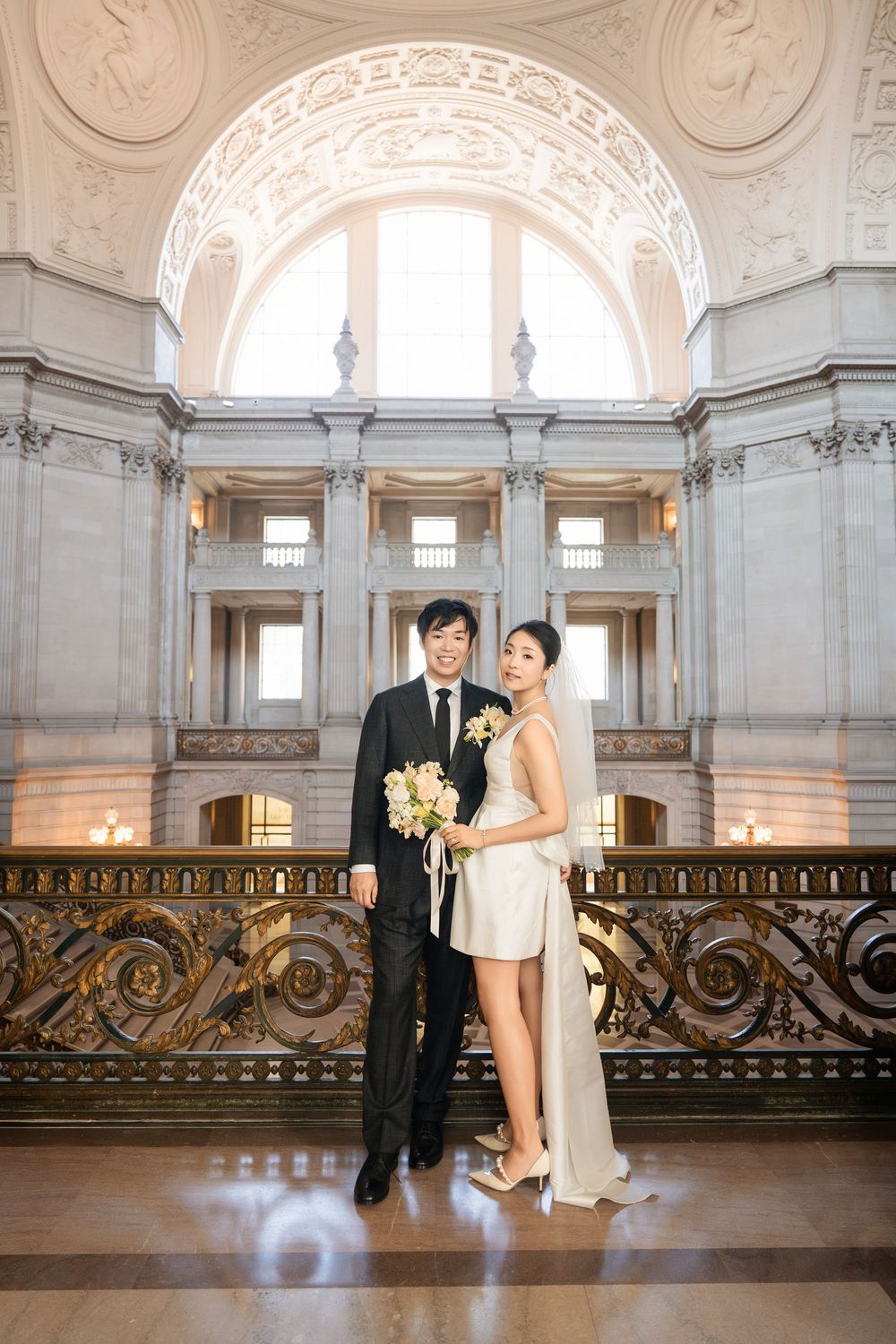 Newlyweds interact playfully in a grand hall with classical architecture and ornate details.