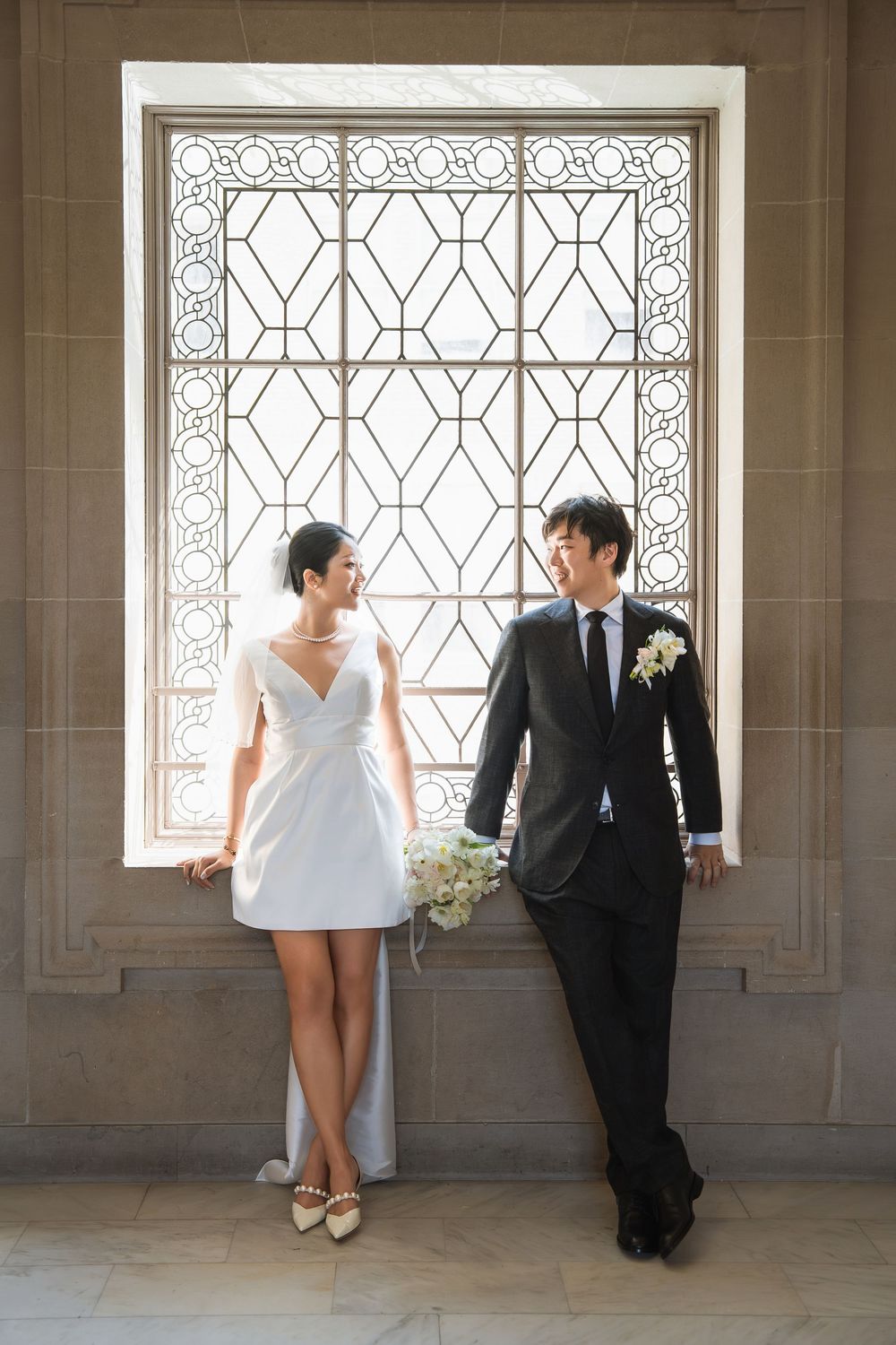 Wedding couple sits together in four artistic poses against ornate windows in a stone hallway.