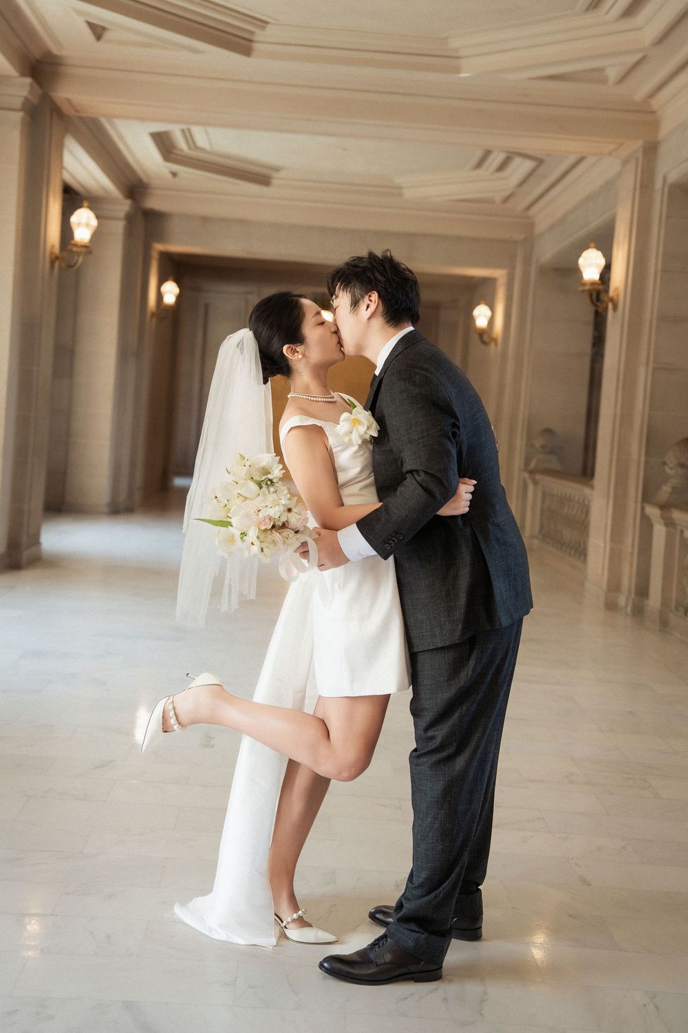 Romantic wedding couple dancing and embracing in an elegant hall with ornate moldings and warm lighting.