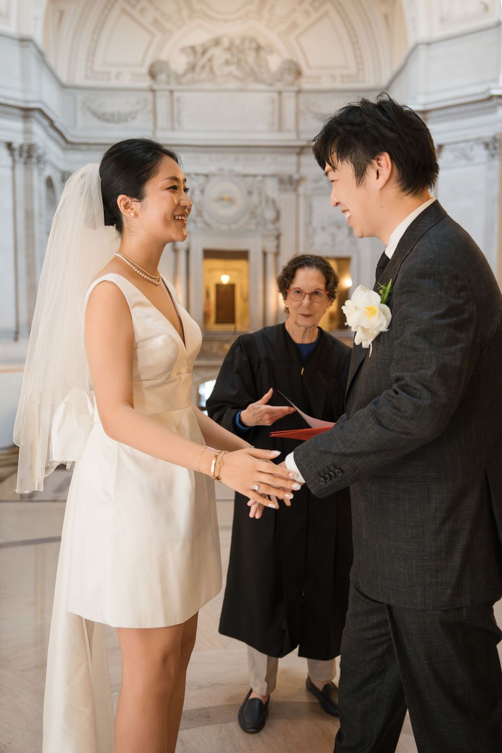 A couple shares an intimate moment during their wedding ceremony in an elegant white marble room.