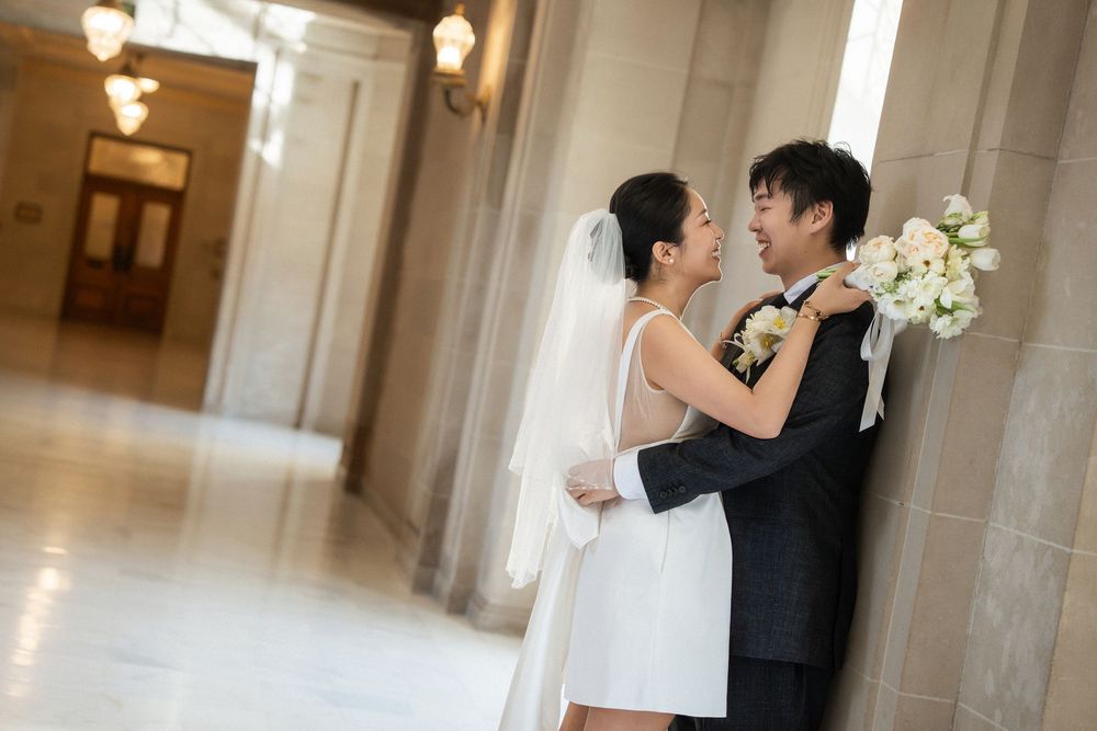 A romantic wedding couple shares a tender kiss in an elegant hallway with soft lighting and classic architecture.