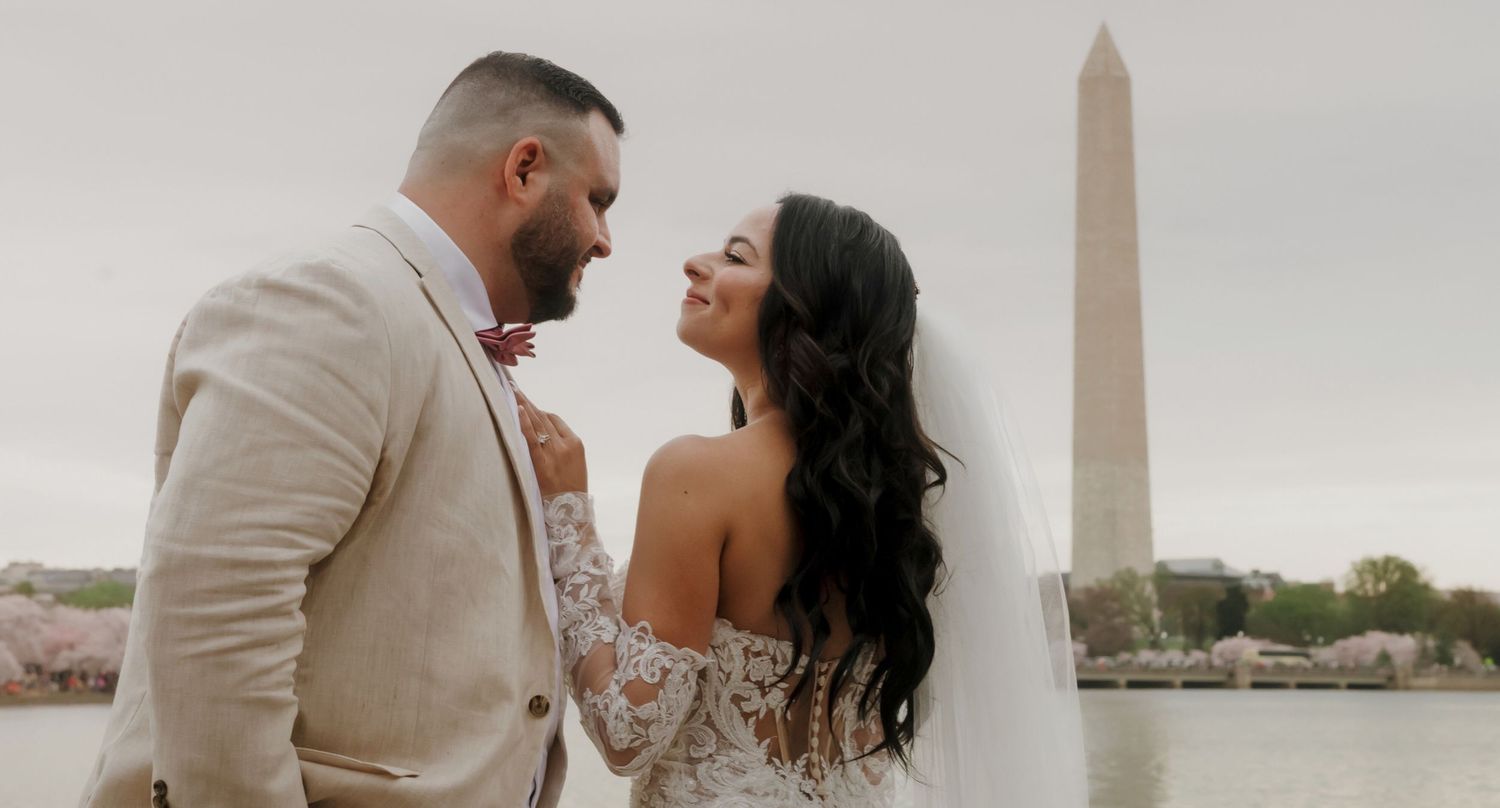 A couple in wedding attire shares a romantic moment against a cloudy sky backdrop.