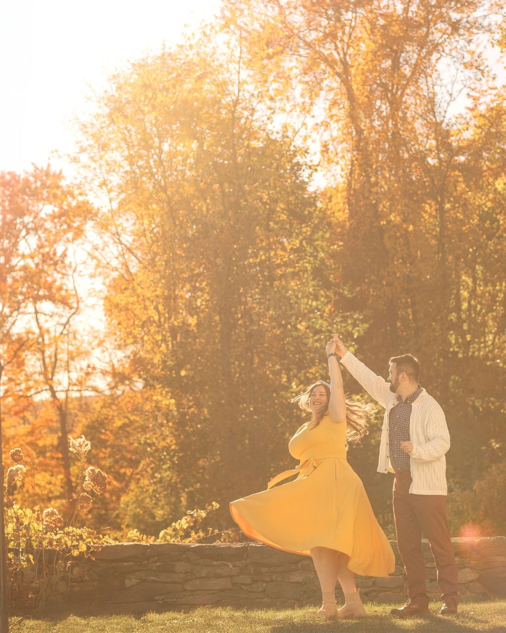 Silhouettes of people dancing and jumping in a park during golden sunset with autumn trees in the background.