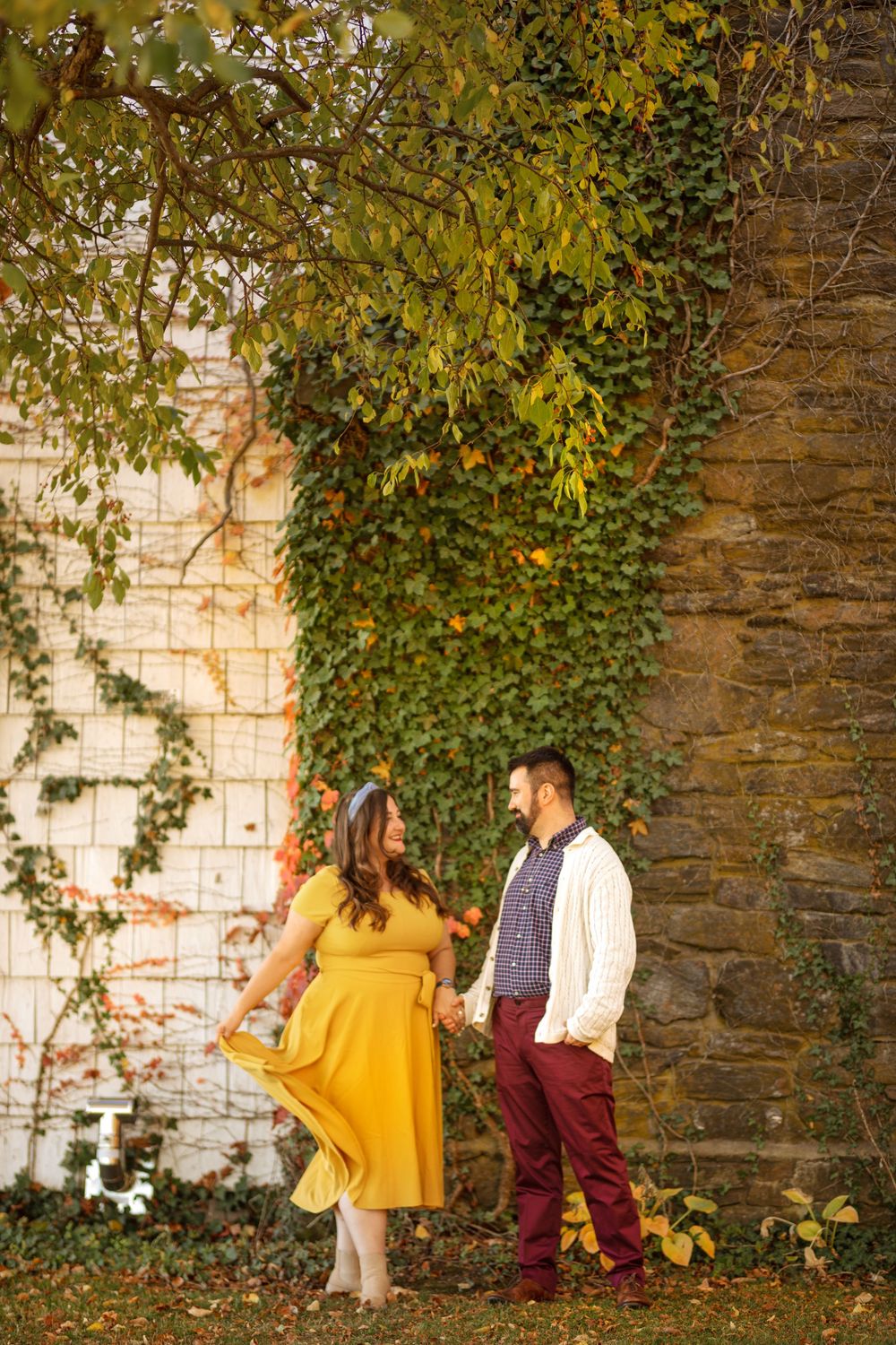 Romantic autumn engagement photo with couple against ivy-covered stone building.