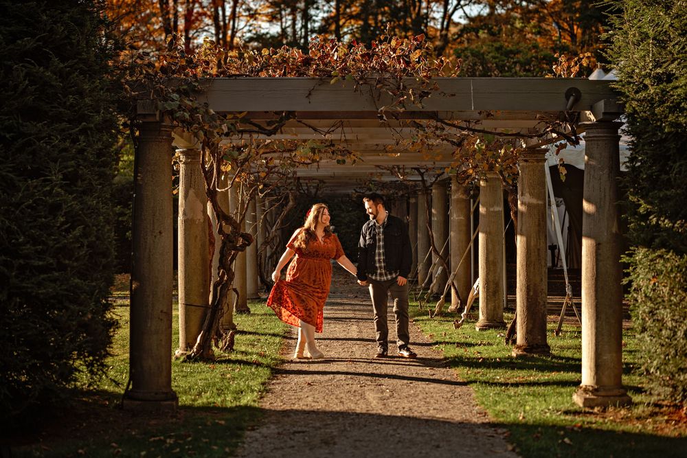 Wedding party walks through autumn garden pathway with stone columns.