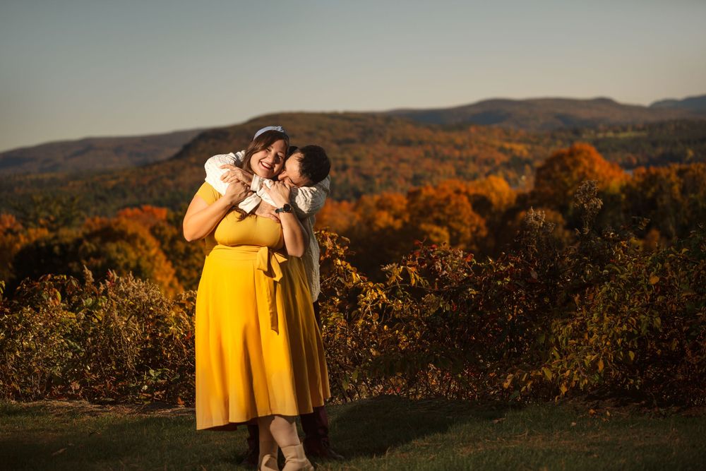Couple embracing against backdrop of autumn mountains with vibrant fall foliage at sunset.