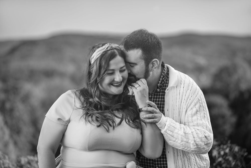 Black and white candid portrait of couple sharing intimate moment against mountain backdrop.