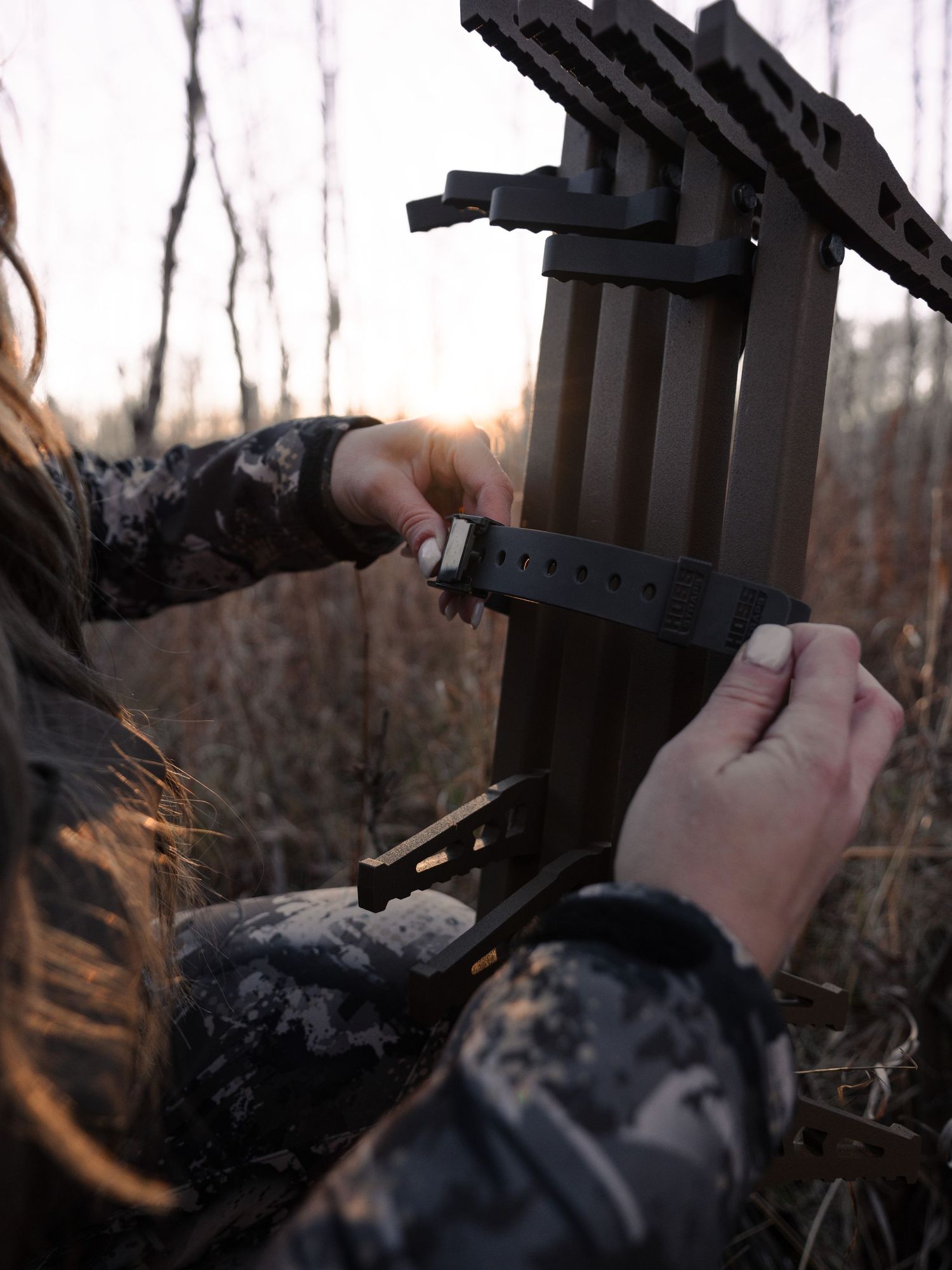 Hands adjusting camera mounting equipment in a wooded setting.