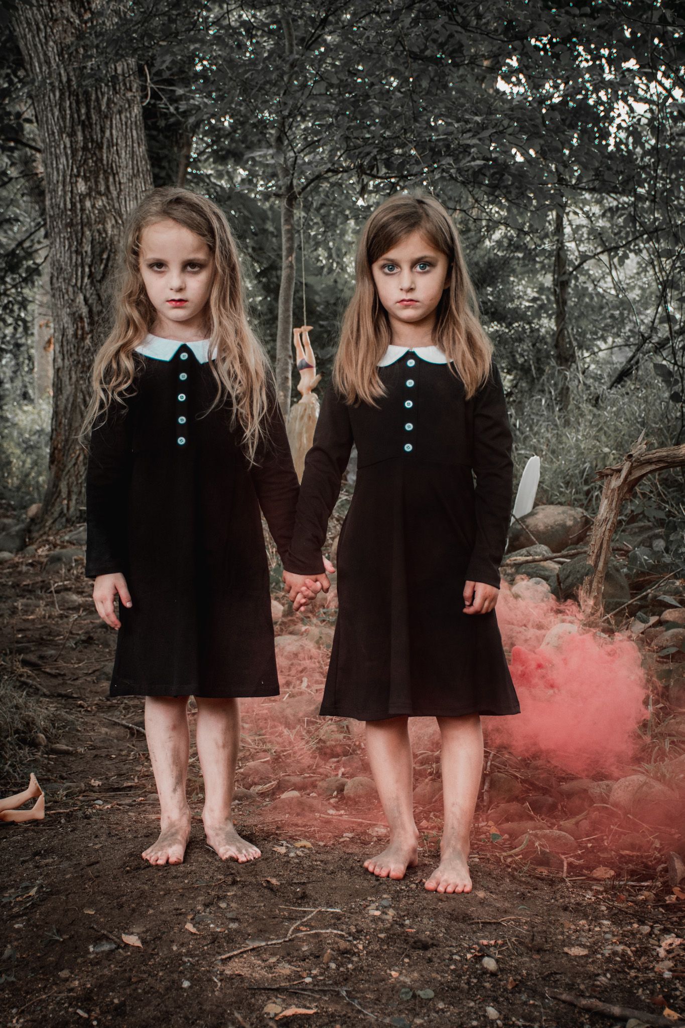 Two girls in matching black dresses in dark forest with pink smoke.