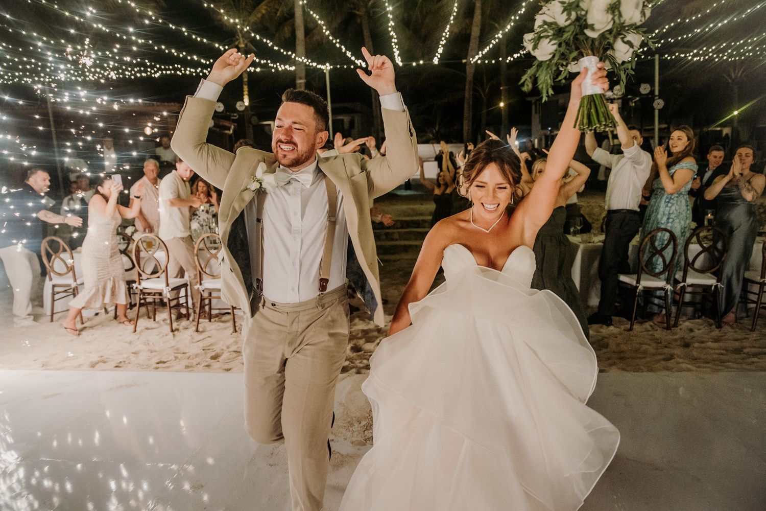 Wedding party dances and celebrates under twinkling lights at an outdoor evening reception. El Dorado Royale Wedding Photographer
