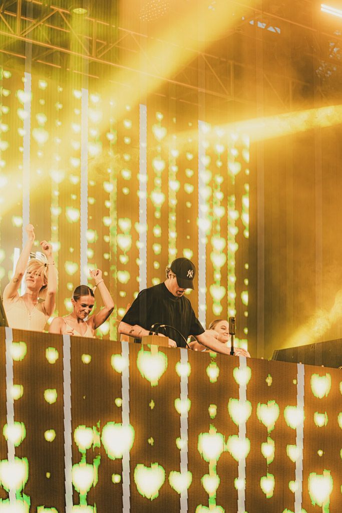 Concert performers on stage behind a wall of glowing golden heart-shaped lights creating a warm atmospheric effect.