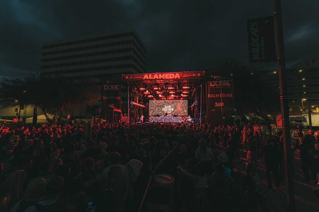 Wide panoramic view of a concert venue with red lighting and distant stage setup in darkness.