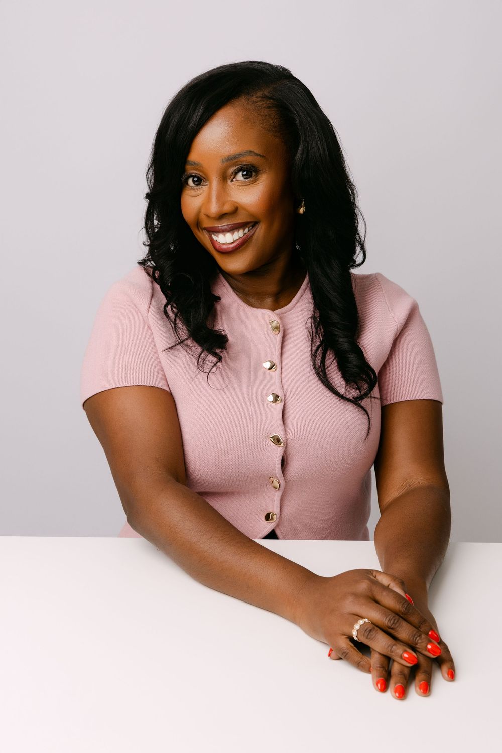Woman wearing pink button-up top smiles warmly during professional headshot session.