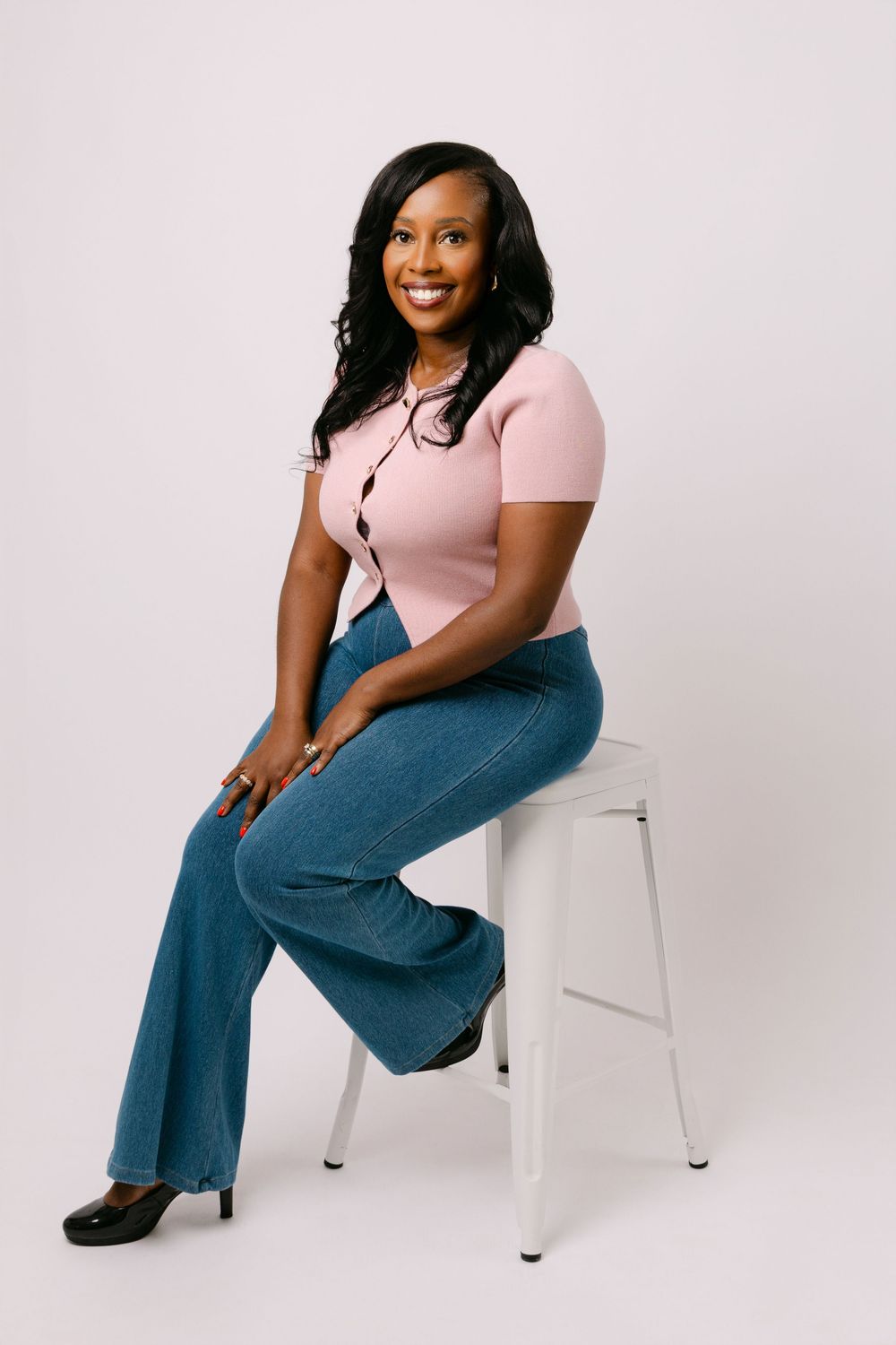 Woman in pink top and jeans sitting on a white stool during studio branding shoot.