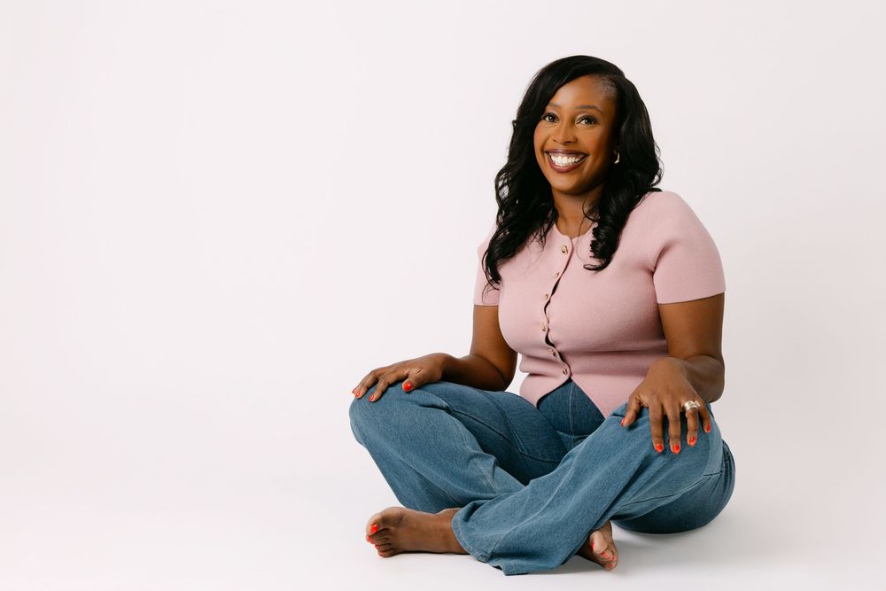 A woman in a pink t-shirt and jeans sitting cross-legged for a branding photography session