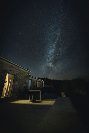 A small illuminated cabin under a starry night sky with the Milky Way visible in the dark wilderness.