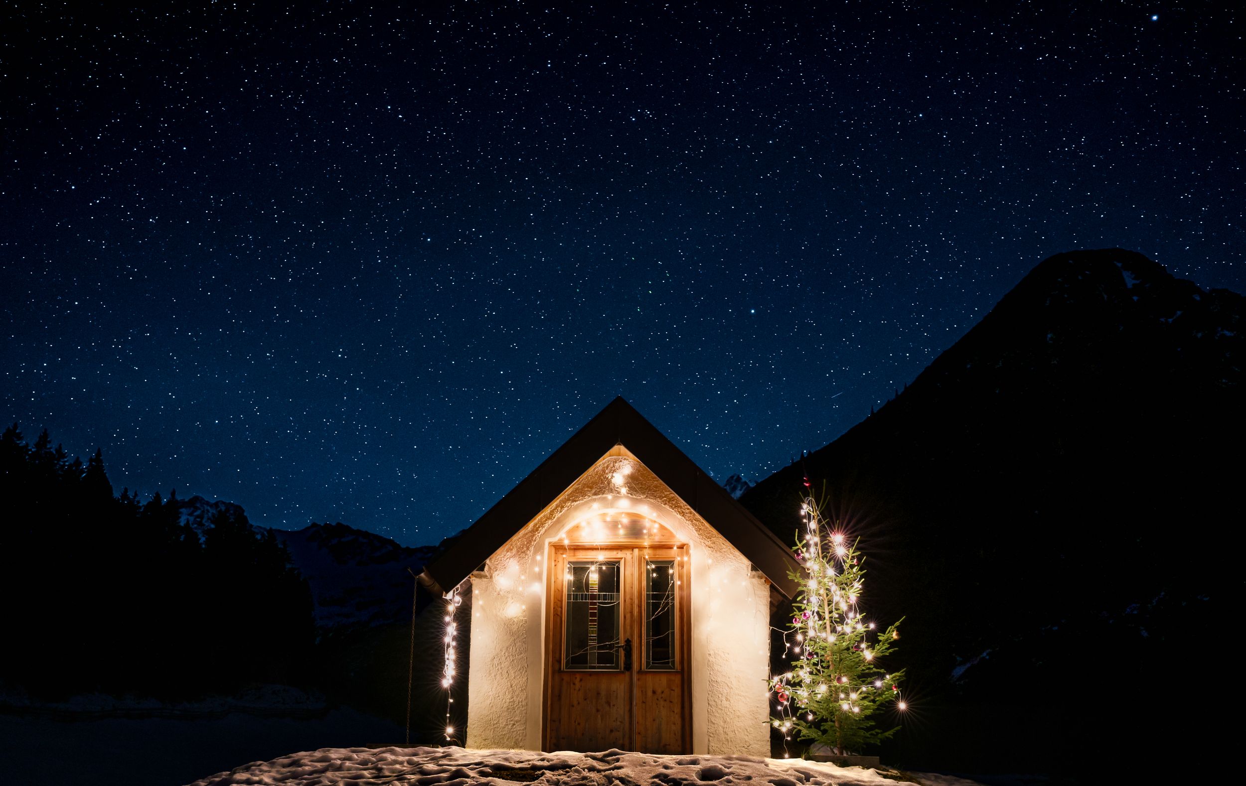 A row of illuminated mountain cabins glowing warmly against a dark night sky with stars visible above.