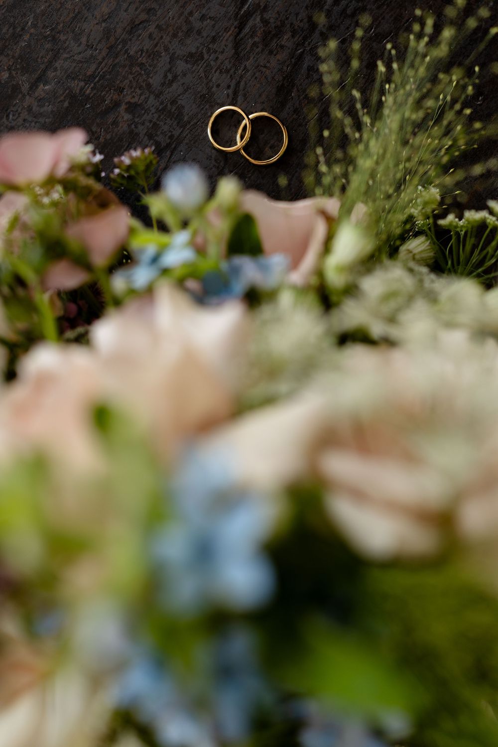 Wedding rings float above blurred floral decorations in a soft focus artistic shot.