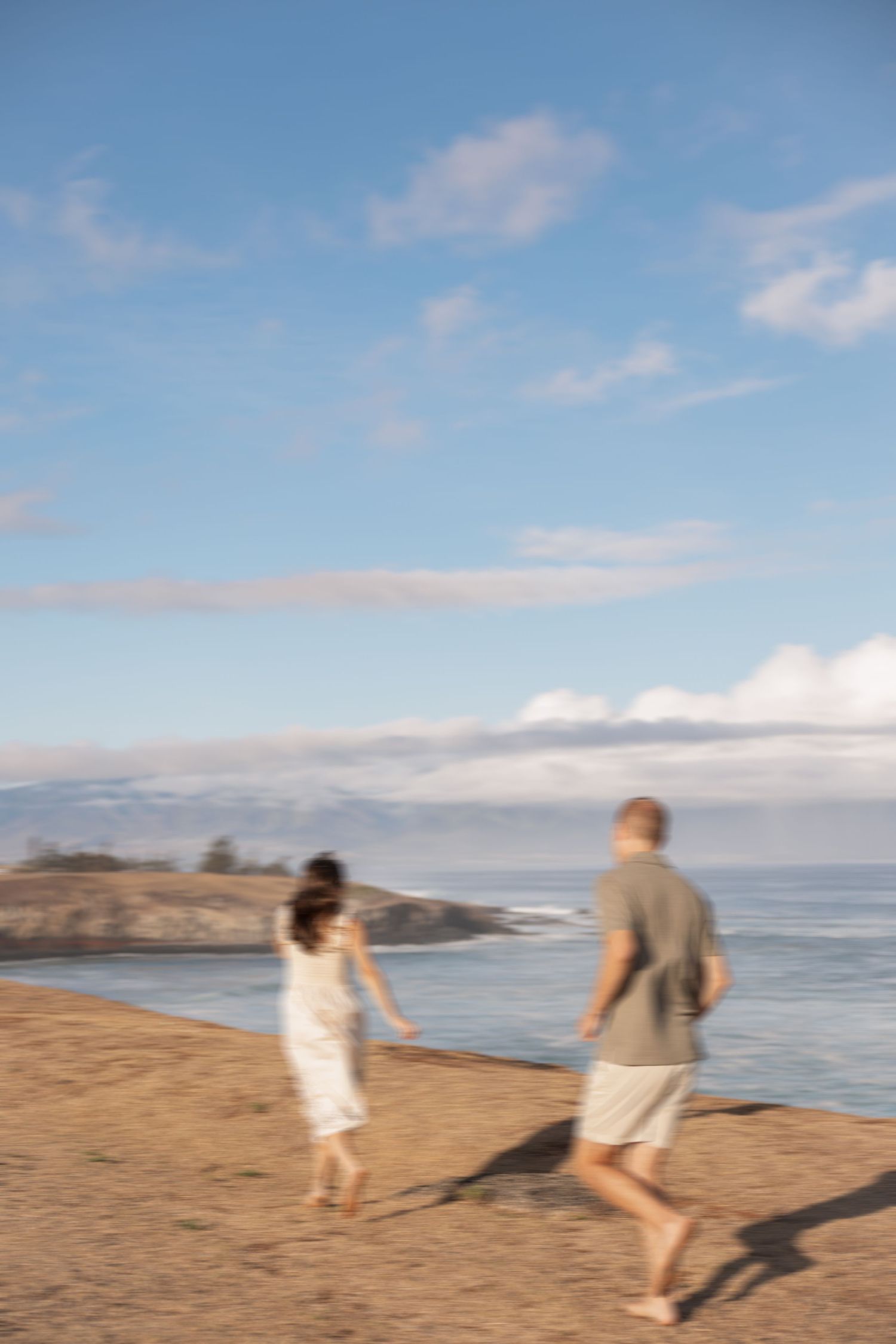 Two people walk together on a sandy beach with ocean views and blue skies on a sunny afternoon.