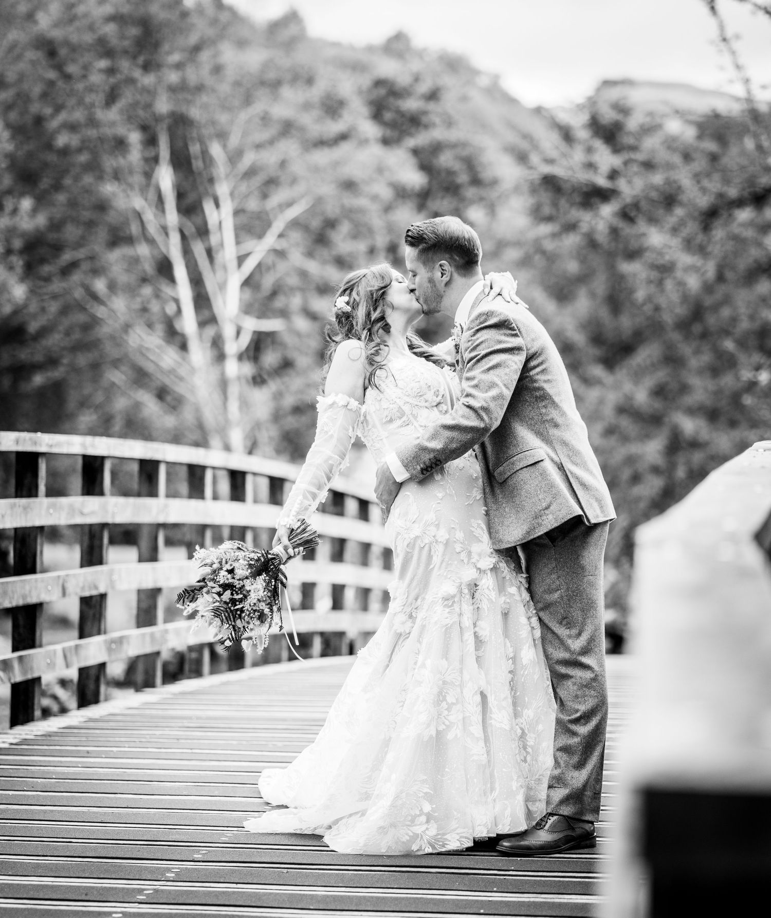 A couple dancing and twirling in formal attire on a wooden bridge with a blurred natural background.