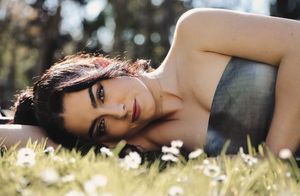 Mujer tumbada sobre césped con flores blancas, iluminada por luz natural entre árboles, sesión de fotos personal en Vitoria, España