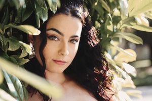 Retrato entre follaje de persona con cabello rizado, iluminada por luz natural filtrada, fotógrafa en Alava