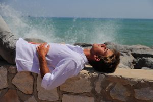 Persona recostada sobre muro de piedra junto al mar, con olas rompiendo y cielo despejado, fotógrafo personal en Vitoria