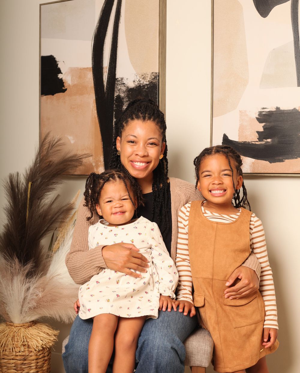 Two children sitting together and smiling while posing for a casual indoor photo shoot.