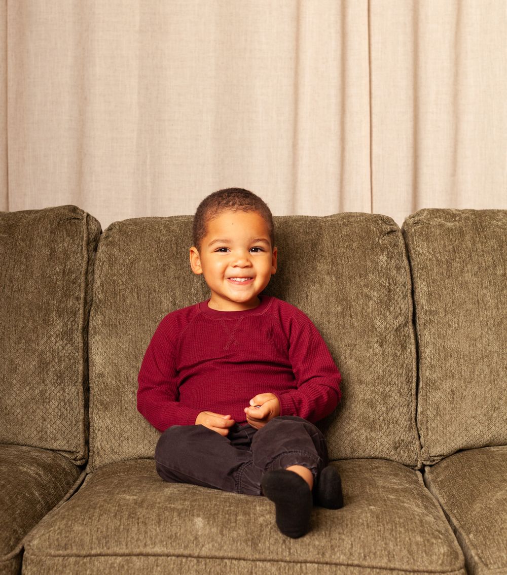 Three children relaxing on a gray couch wearing burgundy and casual attire.