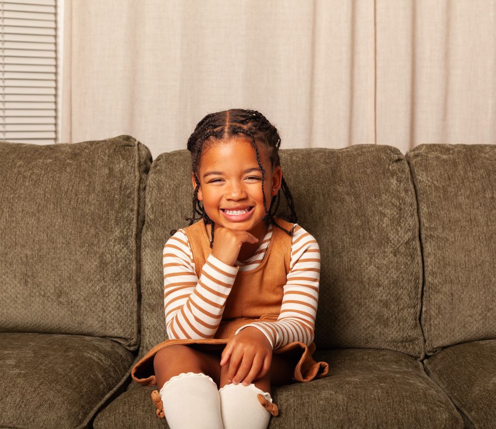 Three children sitting close together on a couch sharing a joyful moment.