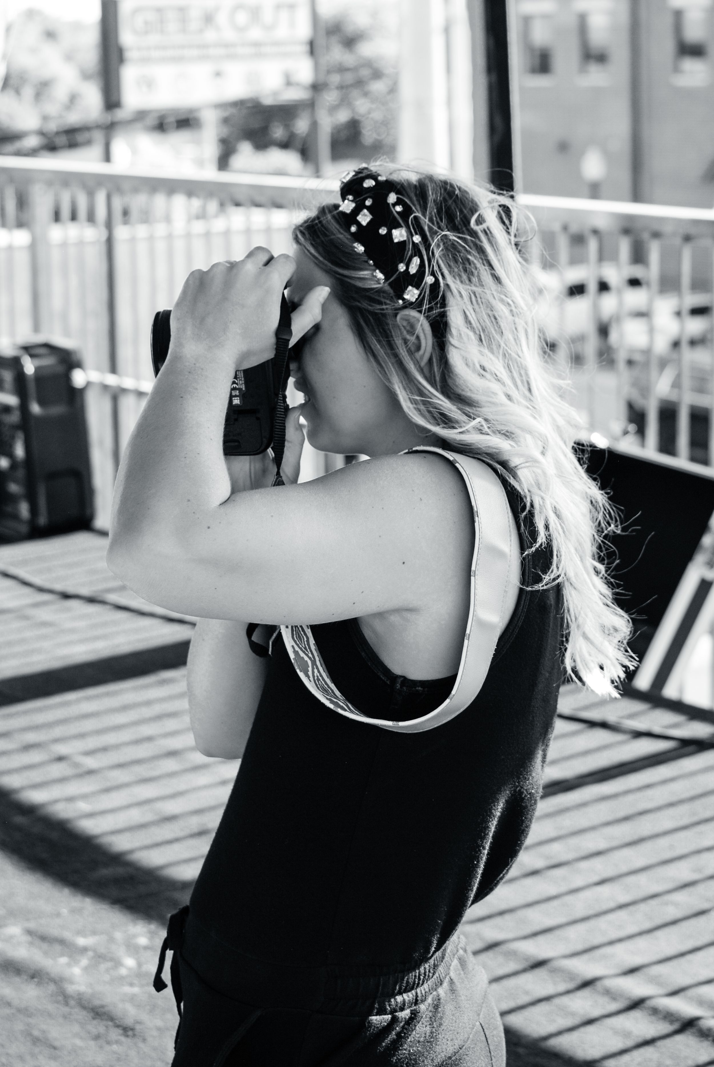 A photographer in a black tank top takes photos on a wooden deck in black and white.