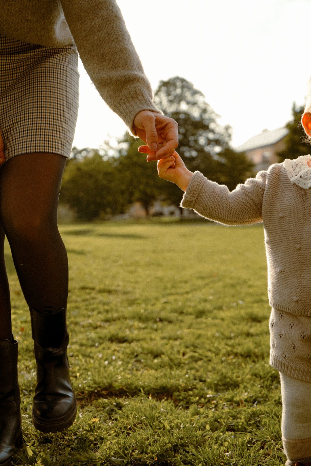 Parent and child holding hands while walking on sunny grass field in autumn.