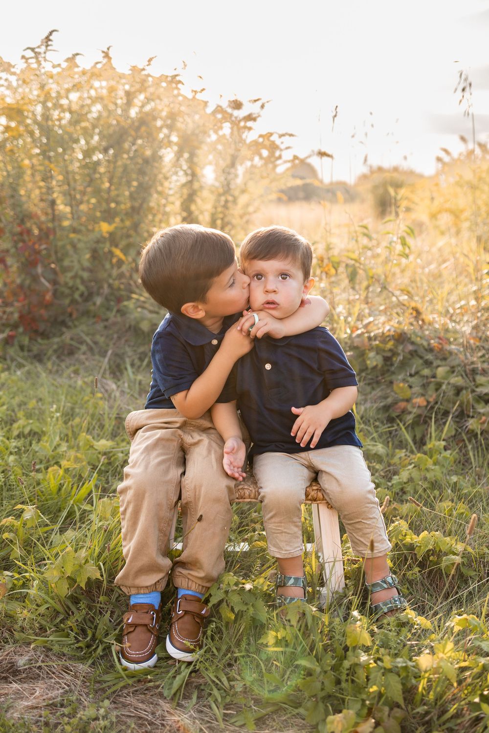 Two young siblings sharing sweet moment while sitting together in grass during sunset. Autumn field during golden hour. Fall Mini Session