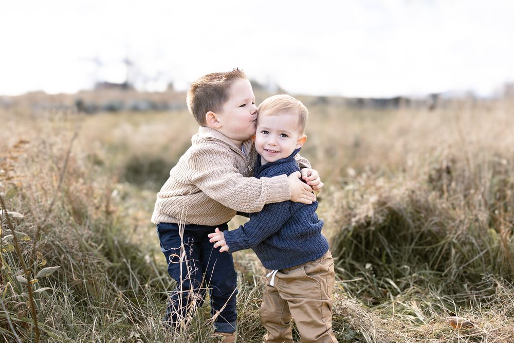 Two siblings share a tender moment while sitting together in a golden autumn field at sunset. Fall Mini Session
