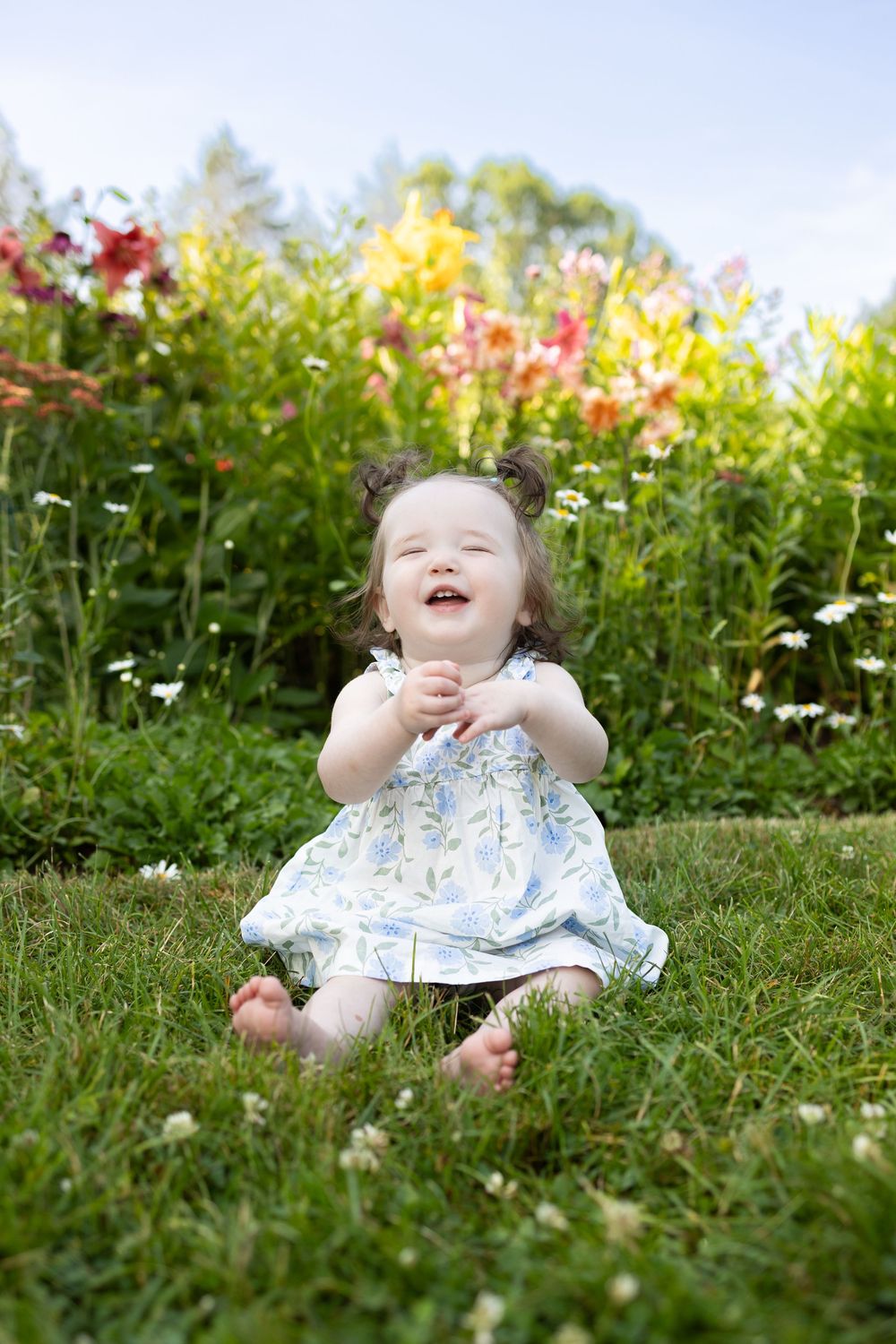 Baby lying in grass surrounded by blooming wildflowers on a sunny day. Spring Mini Session