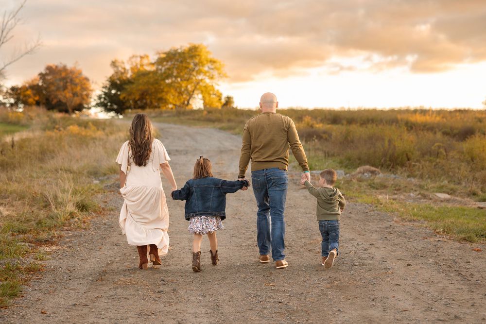 A family walking together on a dirt path during golden hour sunset with warm autumn colors in the background.