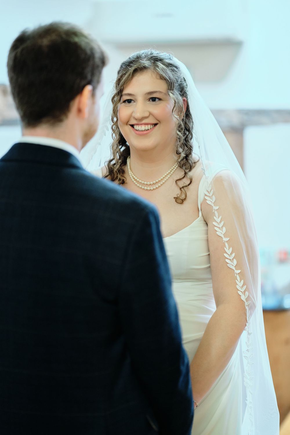 A bride in a white wedding dress with a delicate veil smiles during an intimate wedding ceremony moment.