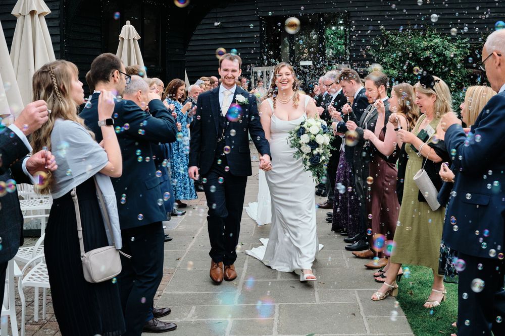 Wedding guests blow bubbles as the newlyweds walk through a celebratory outdoor exit line at a garden ceremony.