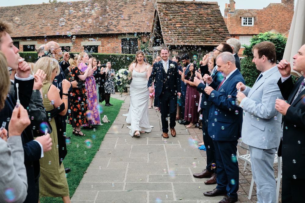 Wedding guests blow bubbles as the newlyweds walk through a receiving line at an outdoor garden reception.