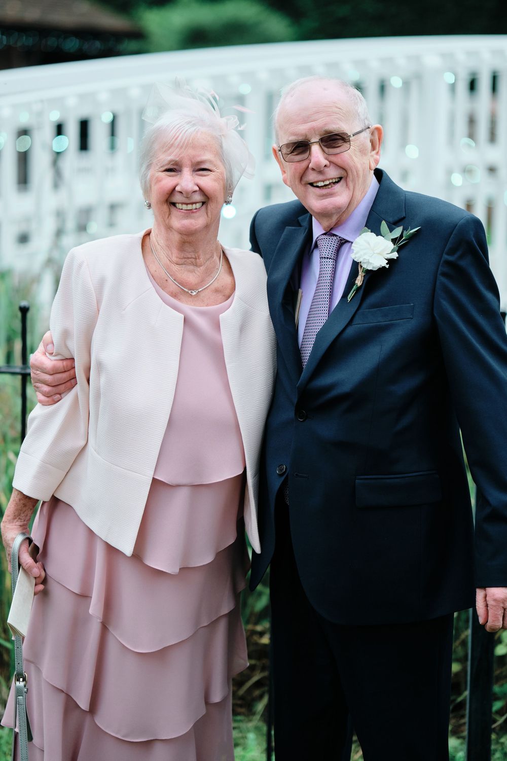 Elderly couple in formal attire sharing joyful moments together at an outdoor event, with the woman in pink and white.