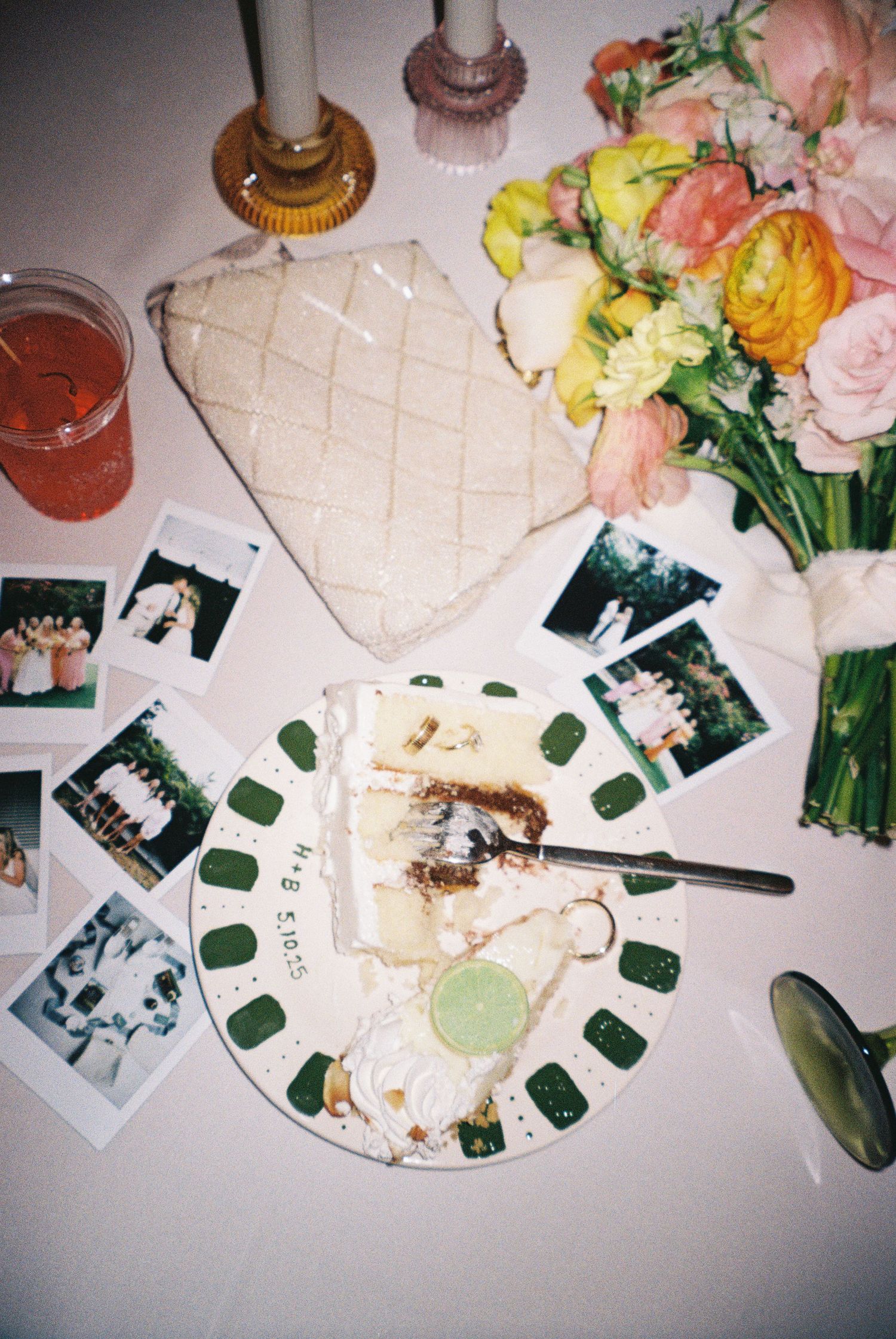 Overhead view of a white heart-shaped cake, colorful flowers, polaroid photos, and a partially eaten dessert plate.
