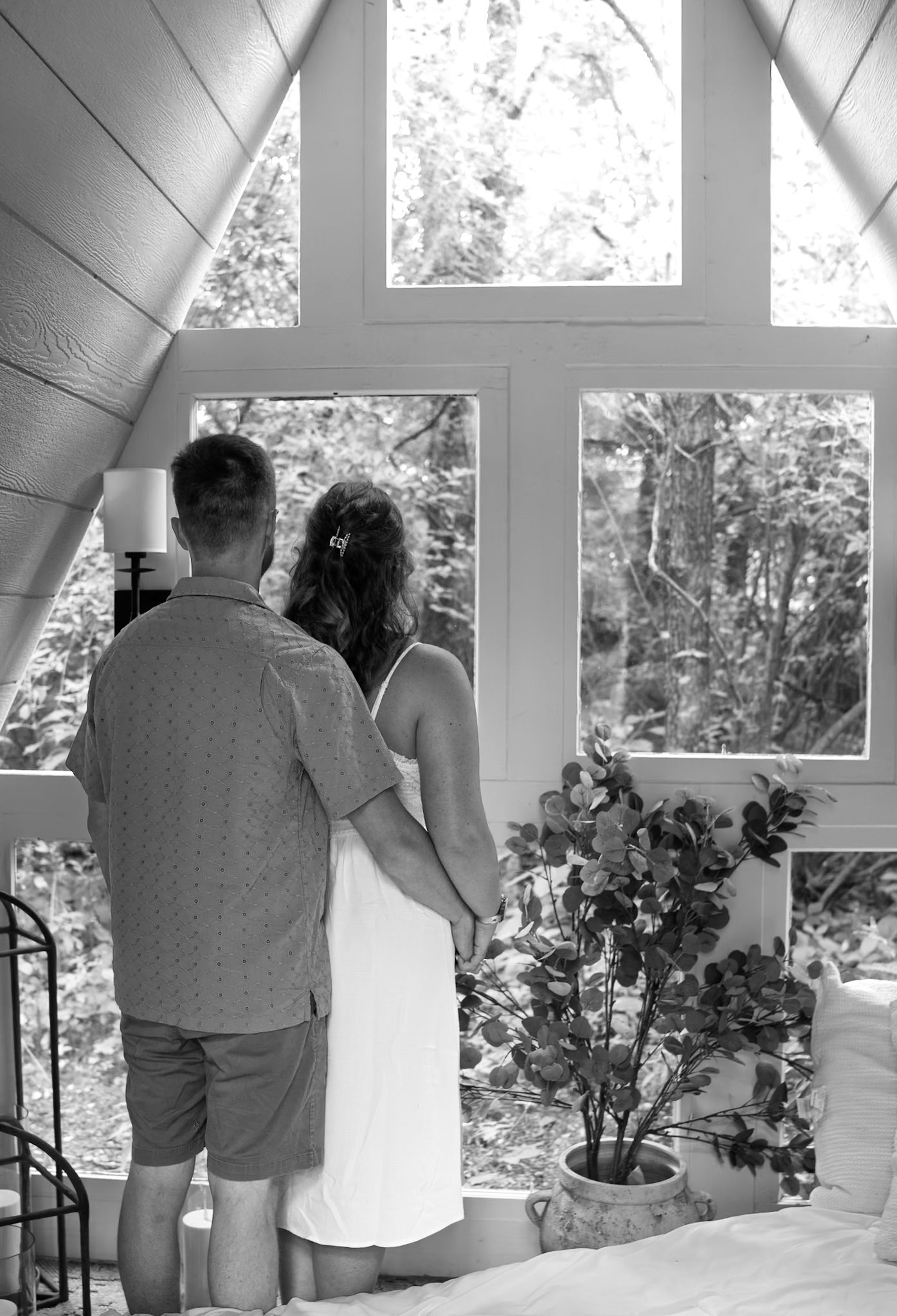 A couple shares a tender moment by a window in black and white photography.