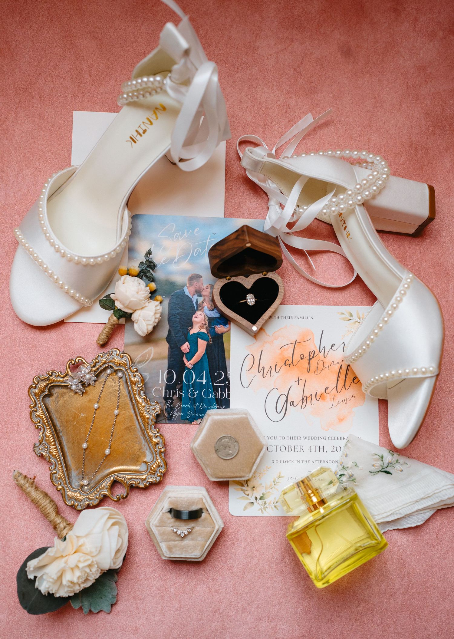 Wedding day details including white shoes, invitations, perfume, and pearl accessories on pink background.